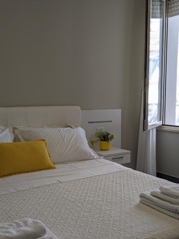 Camera matrimoniale con letto bianco, cuscino giallo e finestra luminosa
