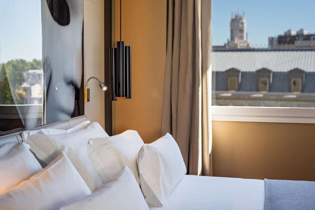 a bedroom with a bed with white pillows and a window at NH Collection Madrid Suecia in Madrid
