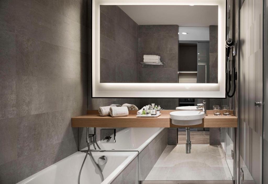 a bathroom with a sink and a mirror and a tub at NH Collection Madrid Suecia in Madrid