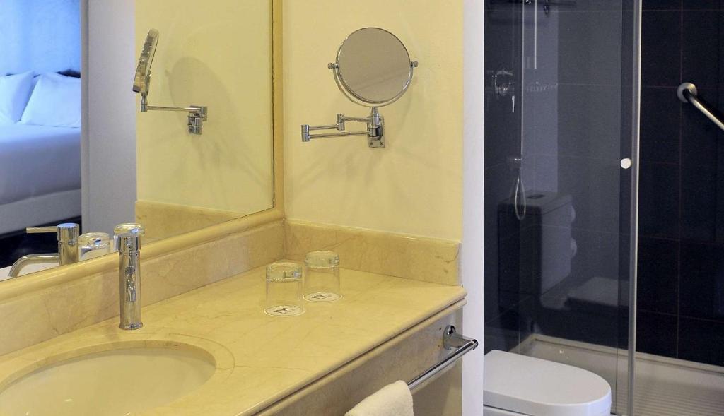 a bathroom with a sink and a mirror and a toilet at NH Ciudad de Santiago in Santiago