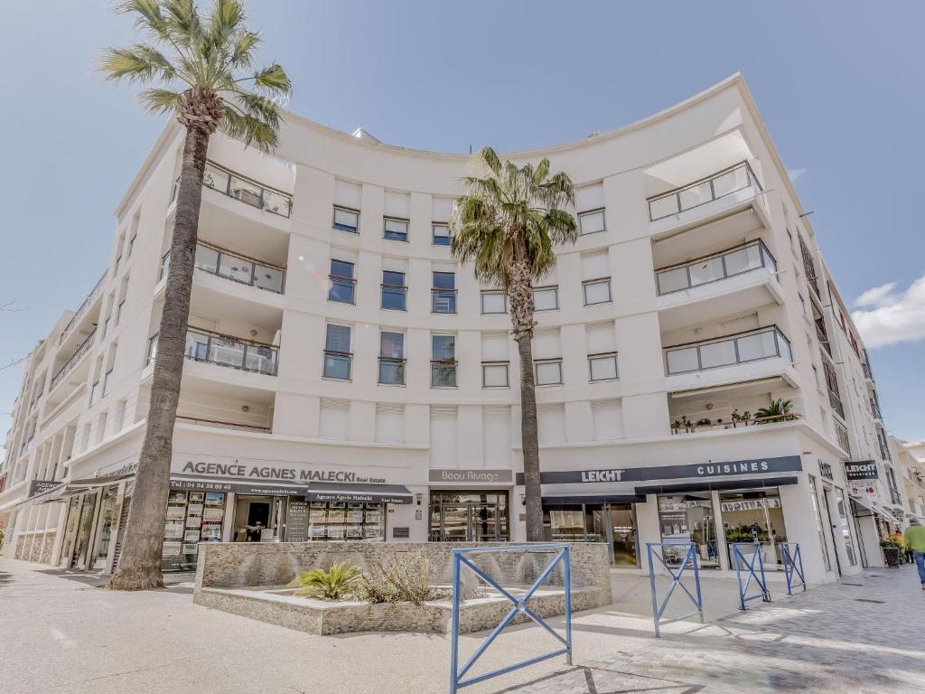 un grand bâtiment blanc avec des palmiers devant dans l'établissement Apartment Beau Rivage-2 by Interhome, à Cavalaire-sur-Mer
