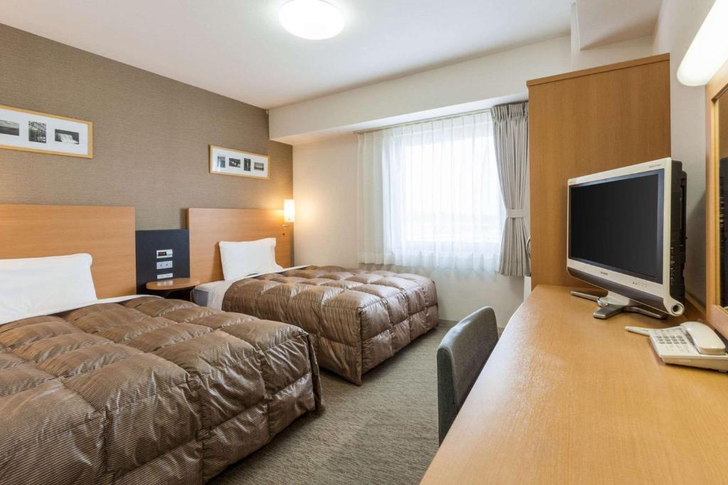 a hotel room with two beds and a flat screen tv at Comfort Hotel Hachinohe in Hachinohe