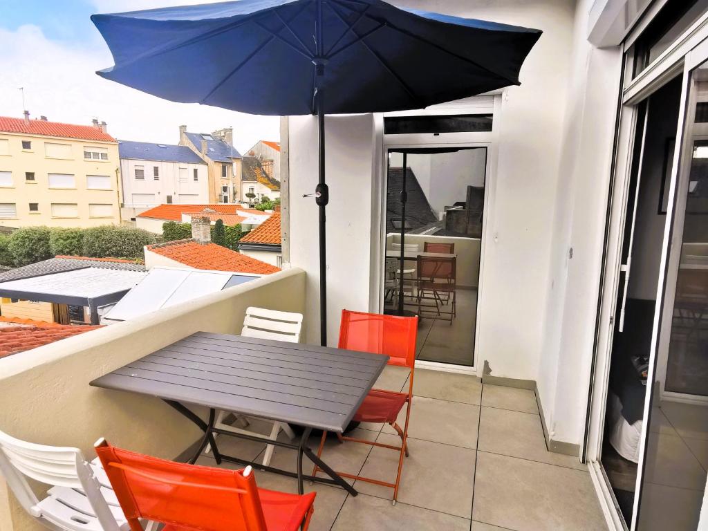 une table et des chaises avec un parasol sur un balcon dans l'établissement Desiree Arago 400m de la Plage, à Les Sables-dʼOlonne
