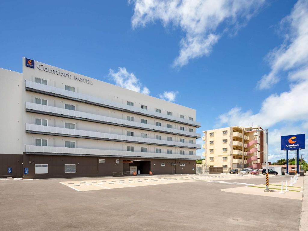 ein großes weißes Gebäude vor einem Parkplatz in der Unterkunft Comfort Hotel Ishigaki Island in Ishigaki-jima