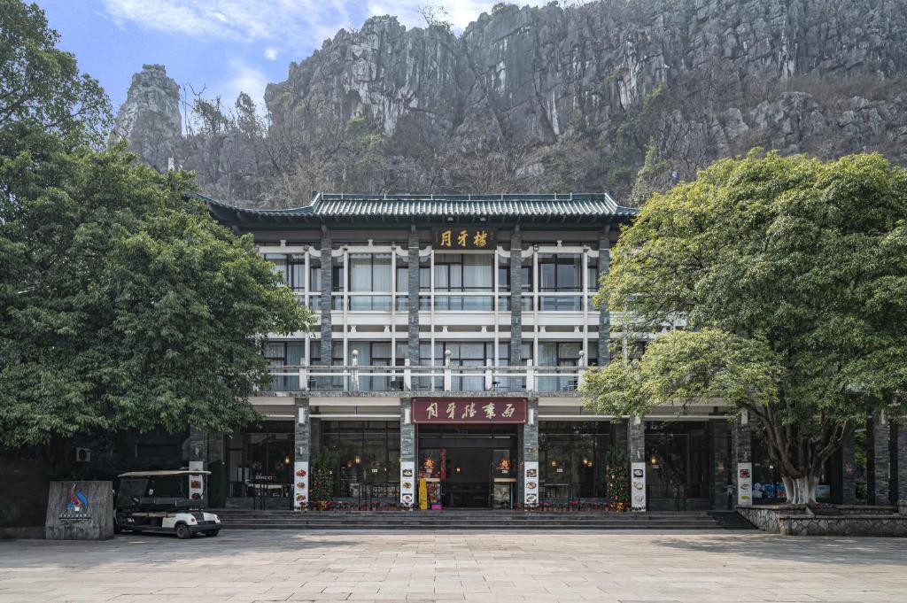 a building in front of a mountain with trees in front at Guilin Crystal Crescent Moon Hotel in Guilin