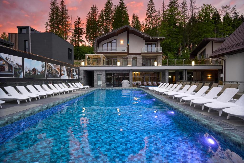 a large swimming pool with white chairs and a house at Karpatski Hotel & Spa in Bukovel