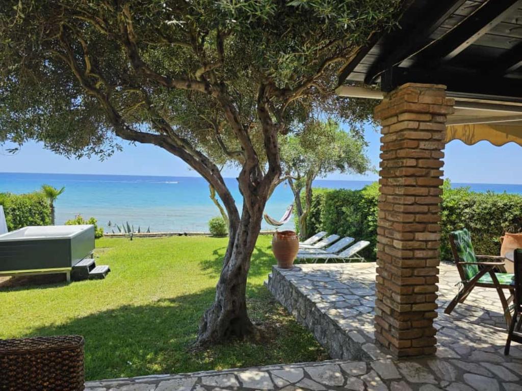 a patio with a tree and the ocean in the background at Corfu Dream Holidays Villas in Glyfada