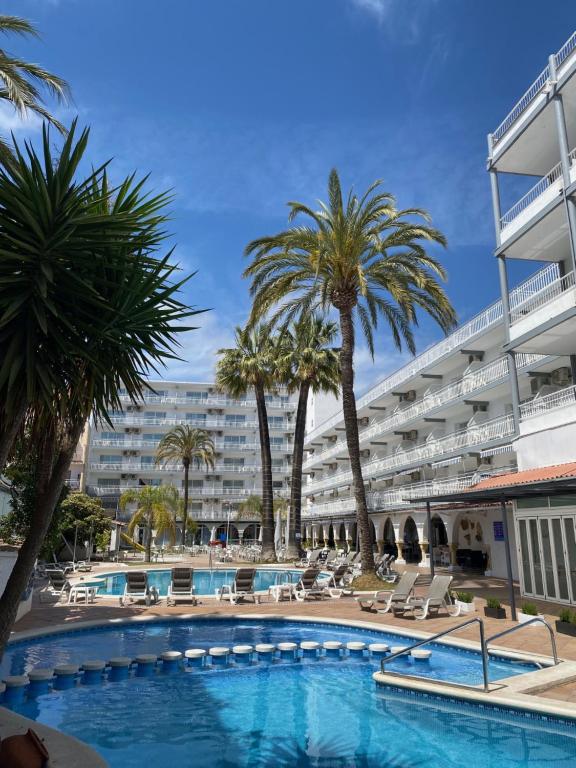 a swimming pool with palm trees and a large building at Hotel Apartamentos Solimar in Calafell