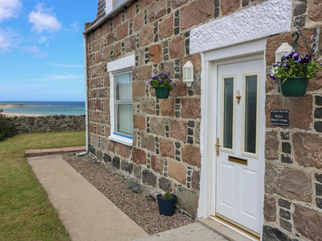 a stone cottage with a white door and two windows at Bella's Beach Cottage in Fraserburgh
