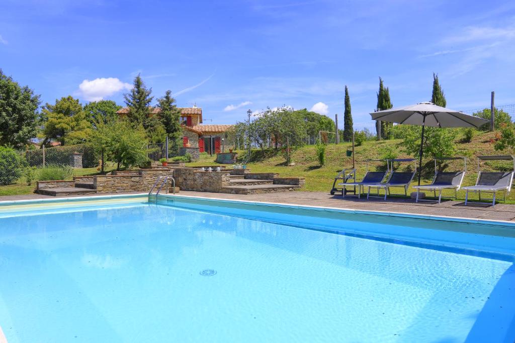 a blue swimming pool with chairs and an umbrella at Casale Cantalena in Cortona