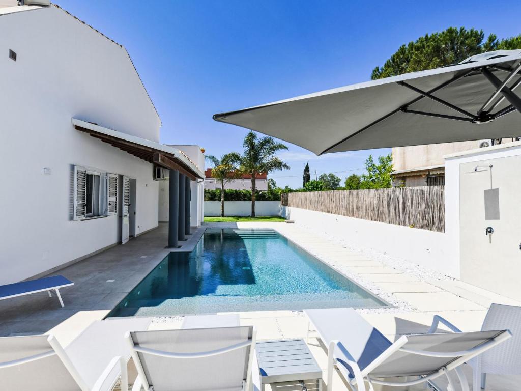 a swimming pool with white chairs and an umbrella at Apartment MareLuna by Interhome in Fontane Bianche