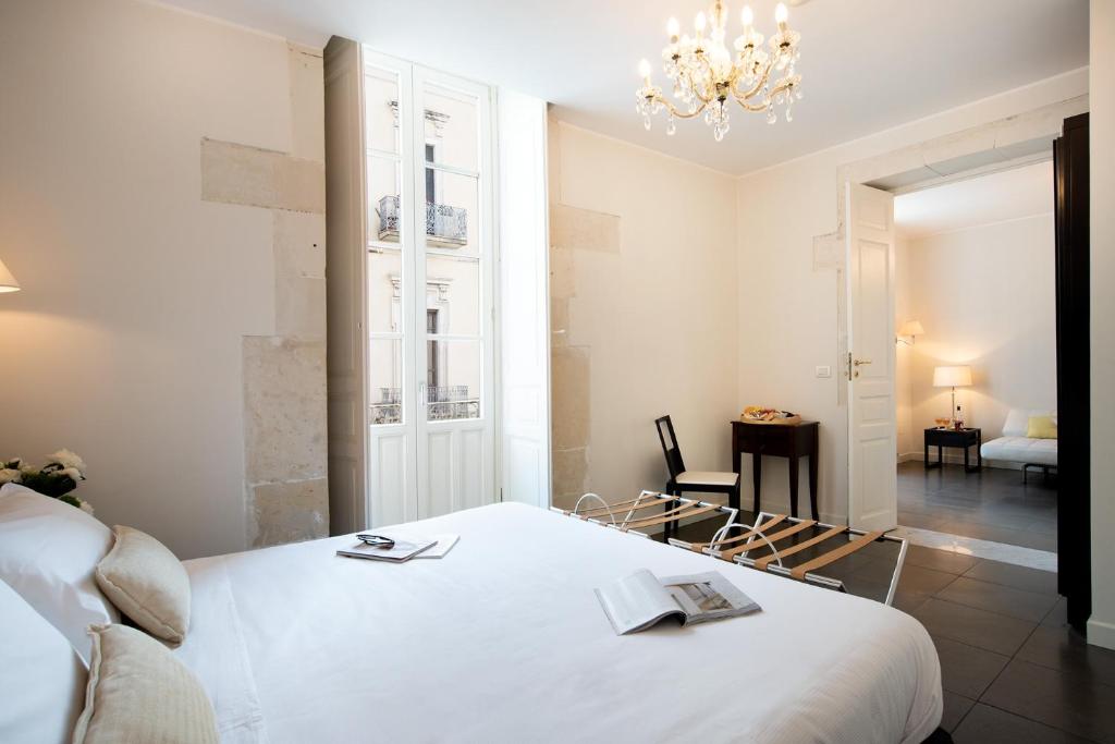 sypialnia z białym łóżkiem i żyrandolem w obiekcie Hotel Palazzo Cavalieri w Syrakuzach