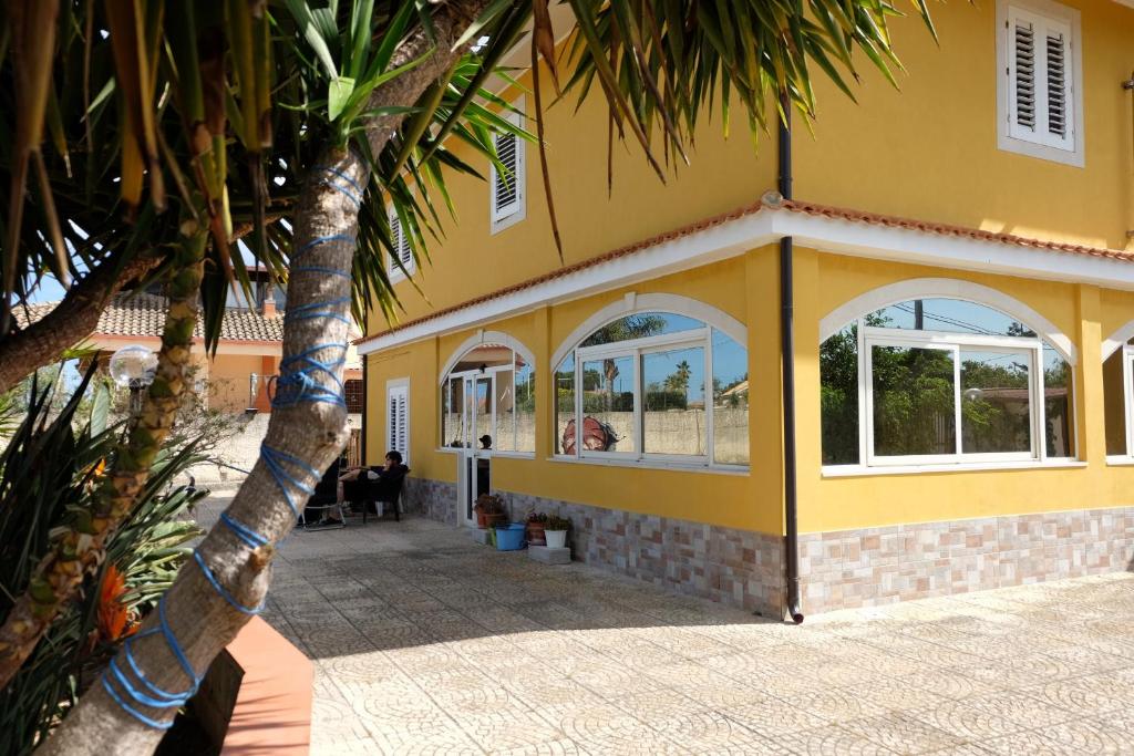 a yellow building with windows and a palm tree at Appartamento in villa al mare in Siracusa