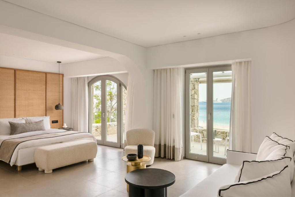 a white bedroom with a bed and a couch and chairs at Grace Mykonos in Agios Stefanos