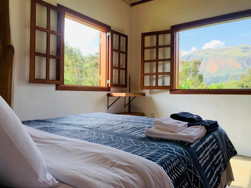 a bedroom with two windows and a bed with towels on it at Chale Vale das Cachoeiras in Capitólio