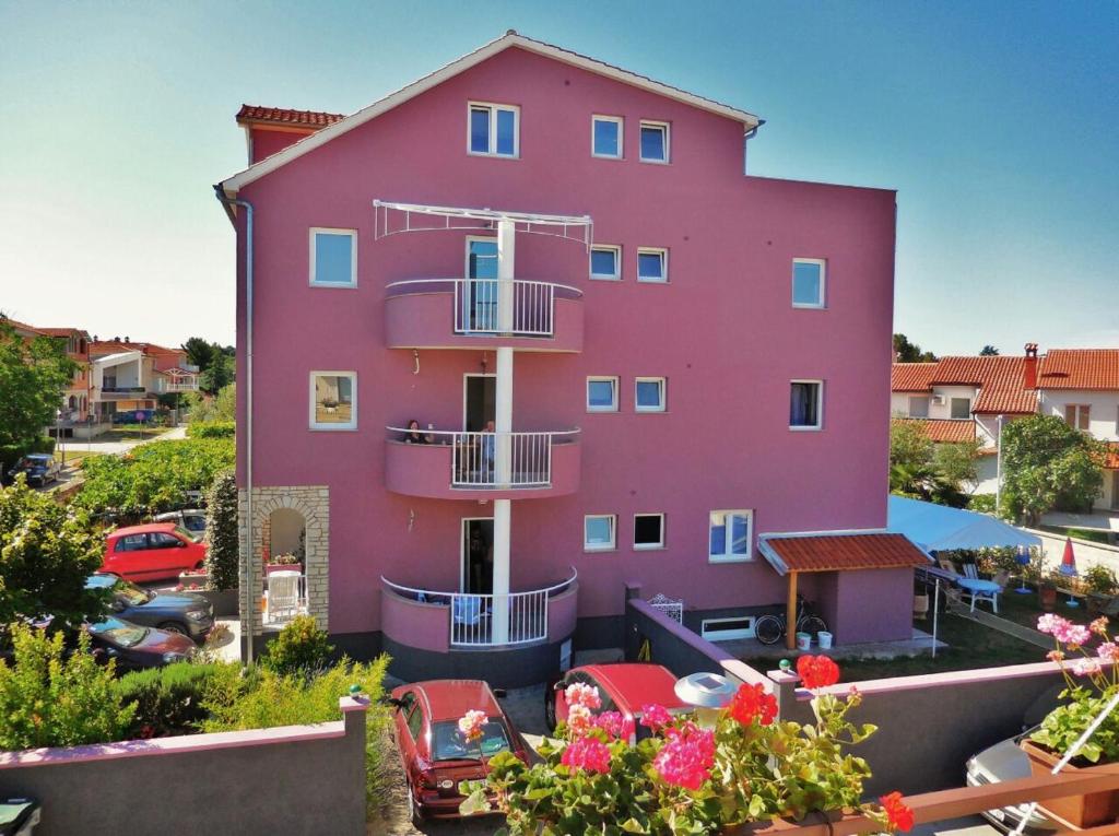 a pink house with cars parked in front of it at Apartments & Rooms Nikolić in Fažana