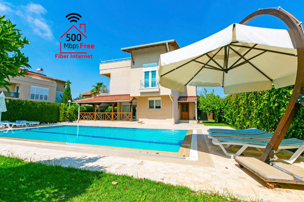 a swimming pool with an umbrella and chairs next to a house at Paradise Town Villa Alison 500 MBPS free wifi in Belek