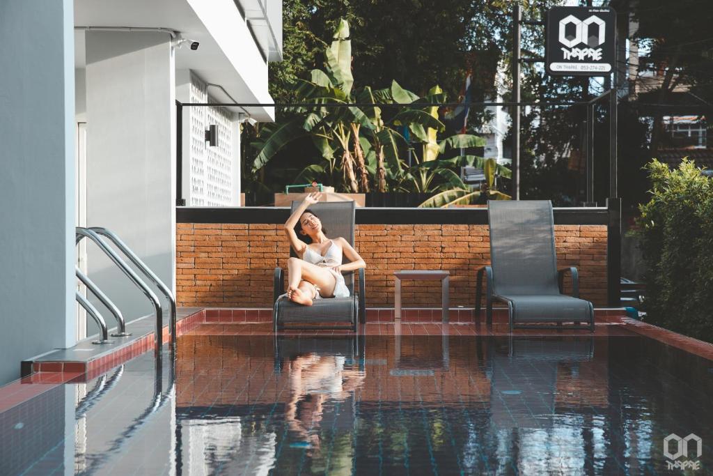 a woman sitting in a chair next to a swimming pool at ON Thapae Chiangmai in Chiang Mai