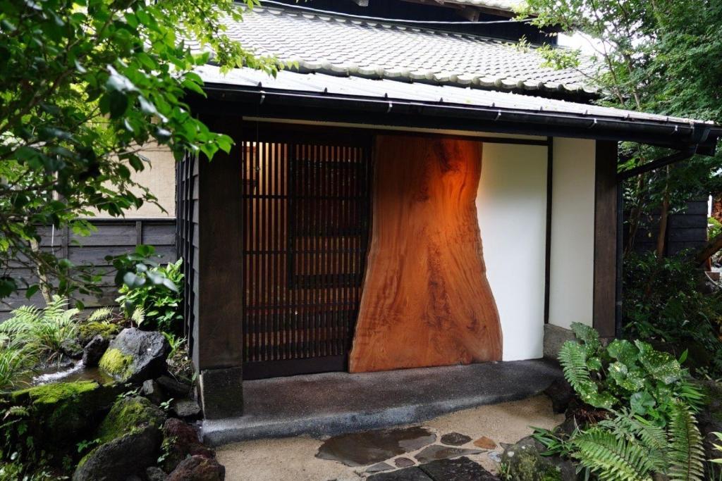 a small shrine with a large tree trunk behind it at 寝室から一望できる阿蘇山の絶景!!築200年の歴史ある米蔵をリノベーションした一棟貸しの宿 in Bōchū