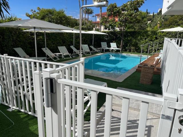 une piscine avec des chaises et des parasols à côté d'une clôture blanche dans l'établissement Résidence Carlton - Entièrement rénové, à Beaulieu-sur-Mer