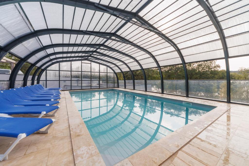 une piscine intérieure avec des chaises bleues et un plafond en verre dans l'établissement Les Demeures du Lac, à Saint-Rémy-sur-Durolle