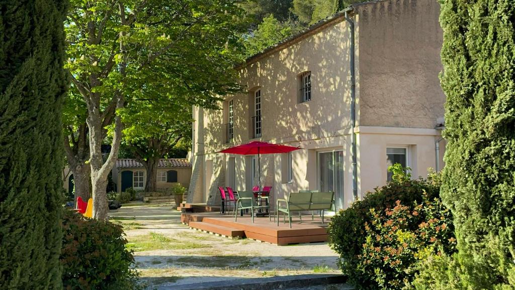un bâtiment avec une table, des chaises et un parapluie rouge dans l'établissement Au calme dans la campagne Aixoise, entouré de cyprès, à Aix-en-Provence