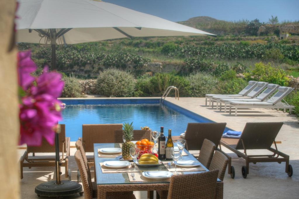 - une table avec des chaises et un parasol à côté de la piscine dans l'établissement Dar il-Wied Farmhouse, à L-Għarb