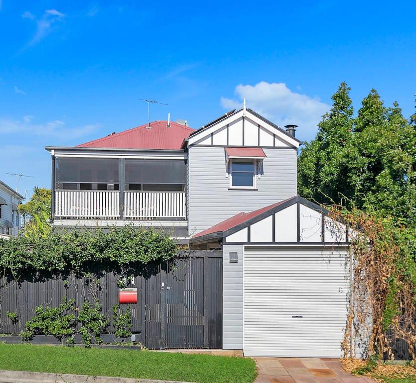 une maison blanche avec un garage et une clôture dans l'établissement Paddington Cottage - A Classic Queenslander Stay, à Brisbane