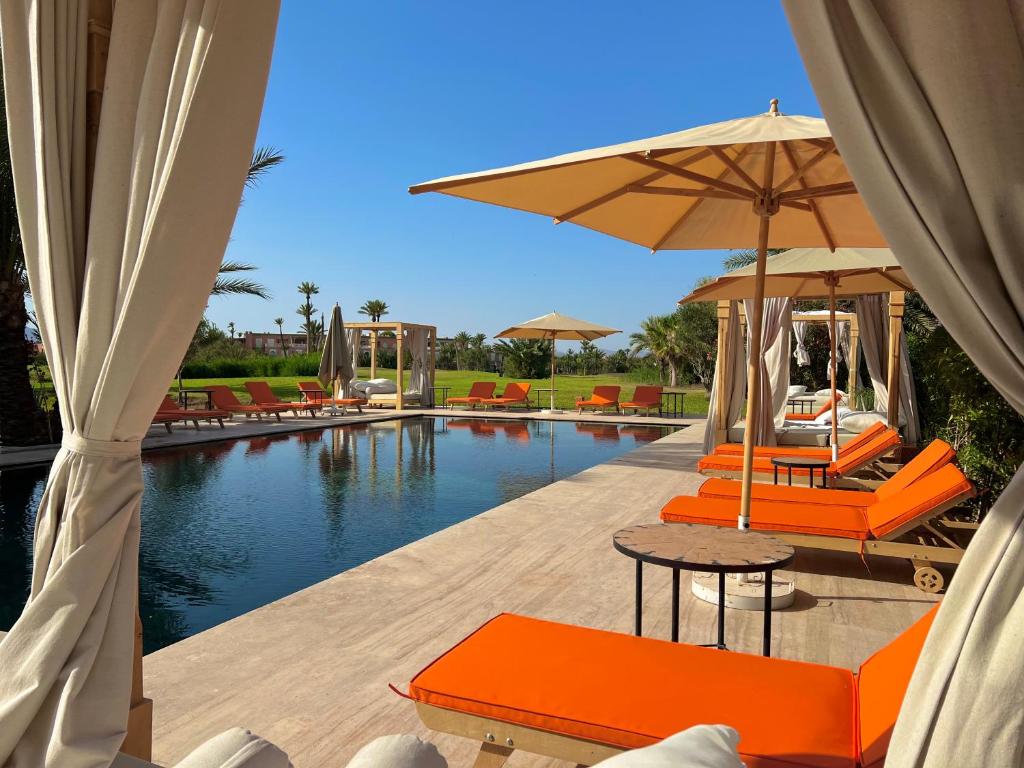 a pool with orange chairs and umbrellas next to a swimming pool at Pavillon du Golf -Palmeraie suites in Marrakech