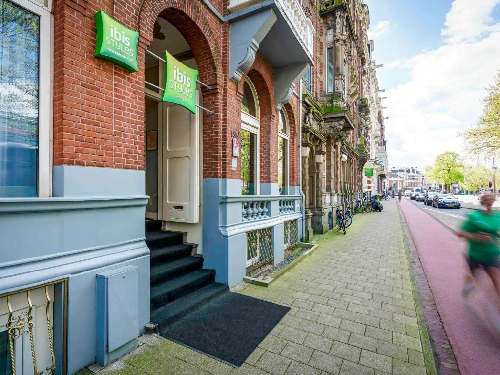 a woman walking down a street in front of buildings at ibis Styles Amsterdam City in Amsterdam