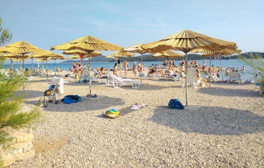 un gruppo di persone seduti su una spiaggia con ombrelloni di Tribunia Beach Hotel a Tribunj (Trebocconi)