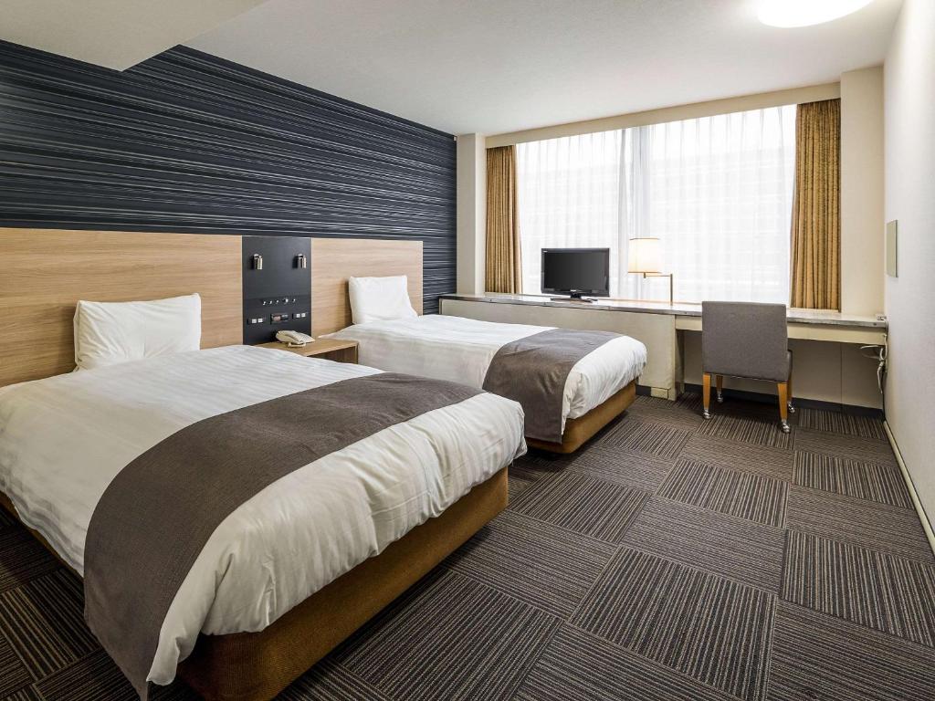 福岡市にあるコンフォートホテル博多のベッド2台とデスクが備わるホテルルームです。