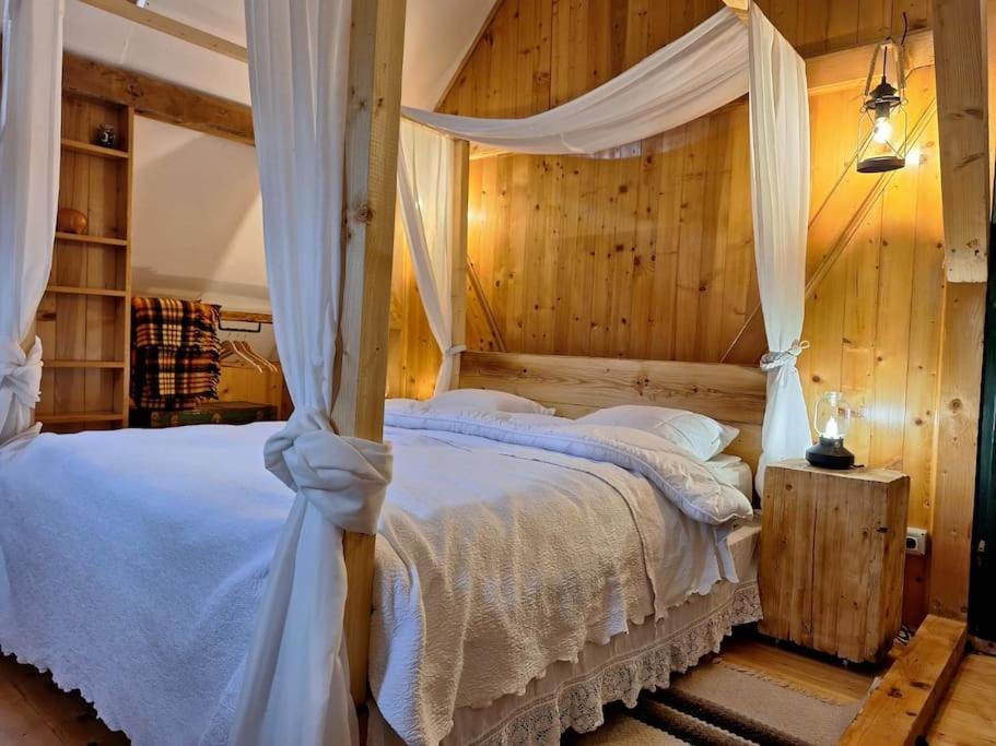 a bedroom with a canopy bed with white sheets and pillows at Căsuța cu Prispă in Sîncraiu
