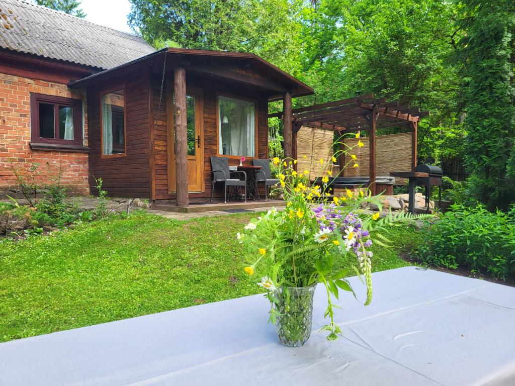 a vase of flowers on a table in front of a cabin at LejasVāgneris in Tukums