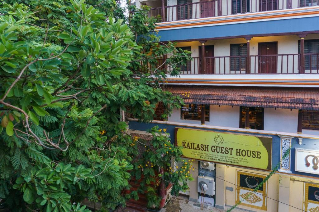 a building with a sign in front of a tree at Kailash Guest House in Puducherry