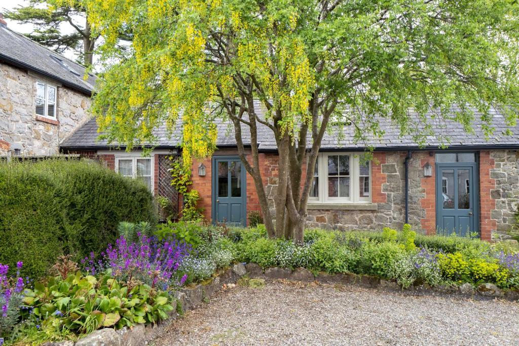 uma casa de tijolos com uma árvore e flores em frente em Courtyard Cottage em Oswestry