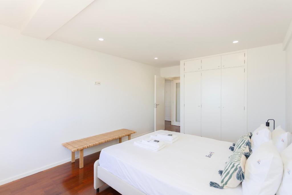 ein weißes Schlafzimmer mit einem Bett und einer Bank in der Unterkunft Liiiving in Matosinhos - Seaside Balcony Apartment in Porto