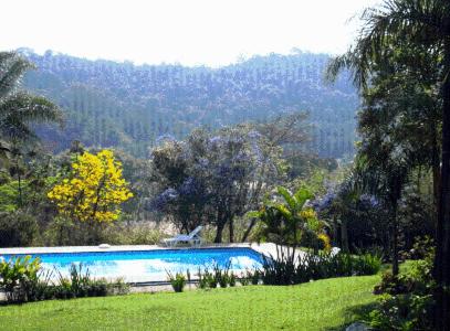 a swimming pool in the middle of a field with trees at Pousada Sapucaia in Guararema