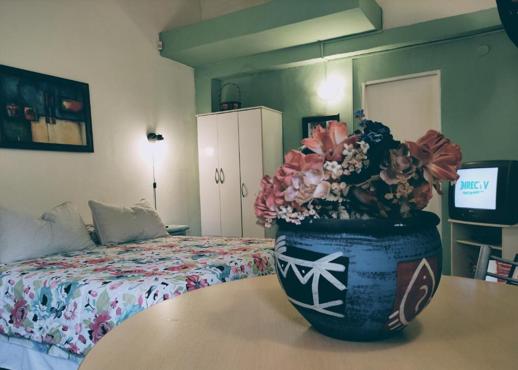 1 dormitorio con 1 cama y un jarrón con flores sobre una mesa en Studios La Bella Vida en Escobar en Belén de Escobar
