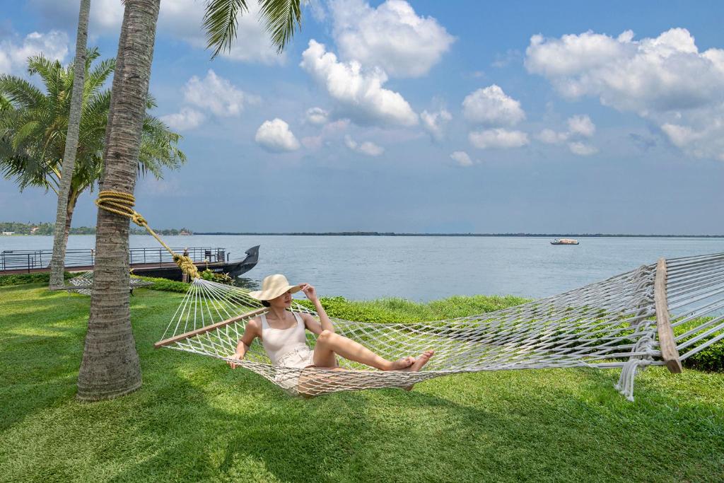 a woman sitting in a hammock next to a palm tree at Kumarakom Lake Resort in Kumarakom