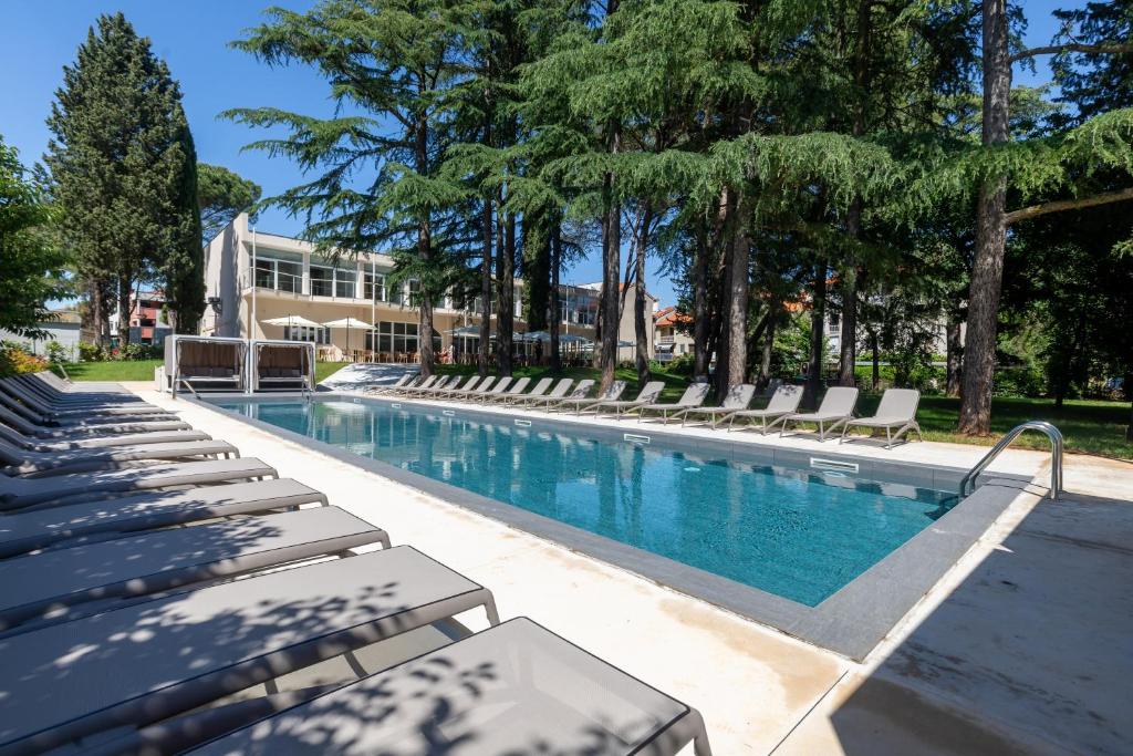 a swimming pool with chaise lounge chairs and trees at Hotel Emaus in Novigrad Istria