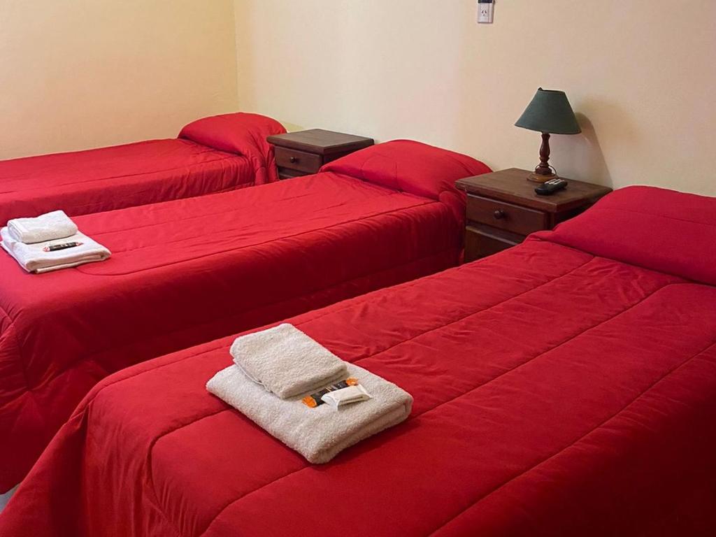 três camas num quarto com lençóis vermelhos e toalhas em Hotel Sol em Termas de Rio Hondo