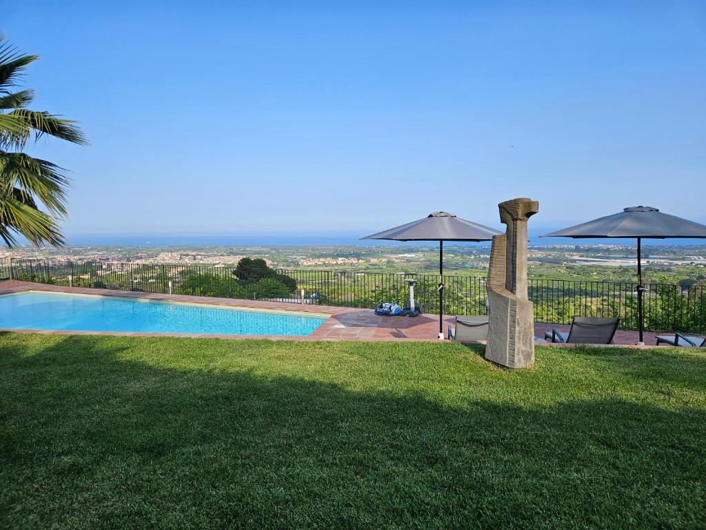una piscina con 2 sombrillas en el césped en Open Land Holiday House, en Fiumefreddo di Sicilia