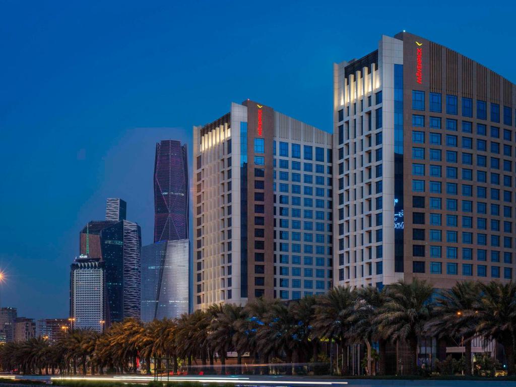 Movenpick Hotel and Residences Riyadh في الرياض: أفق المدينة مع أشجار النخيل أمام المباني