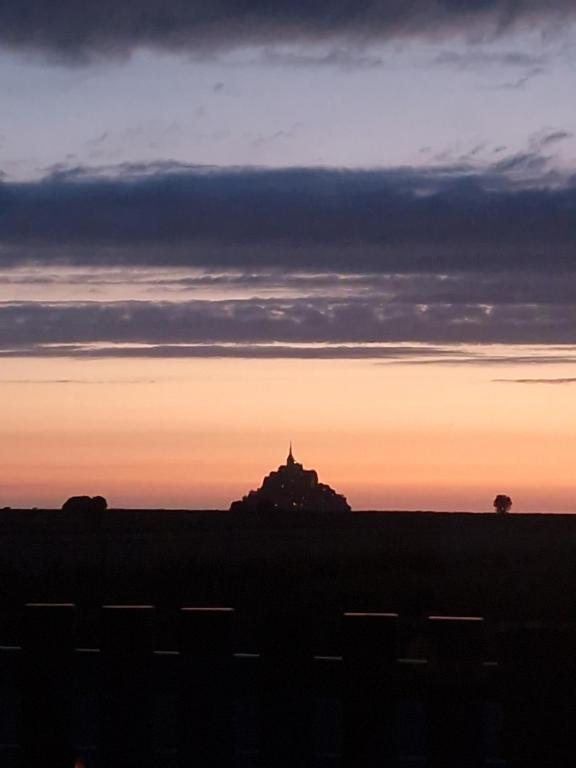une silhouette d'un bâtiment dans un champ au coucher du soleil dans l'établissement Vue sur le Mont St Michel, Grand confort et bien équipé, à Huisnes-sur-Mer