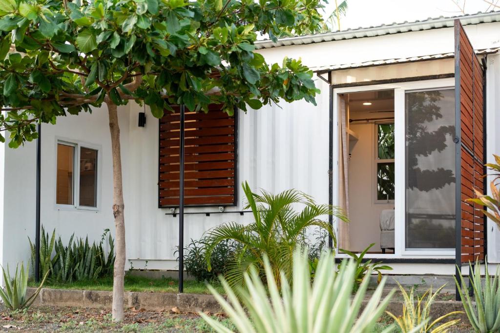 uma casa branca com persianas de madeira e uma árvore em Casa para 4 personas con A/C a 200 mts de la playa Low Tide - Popoyo Aparts em Tola
