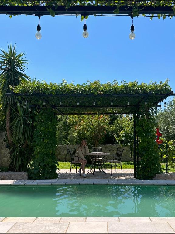 a woman sitting at a table under a pergola next to a pool at Hotel Opera Jaz in Budva