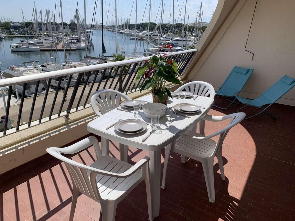 une table et des chaises blanches sur un balcon avec un port de plaisance dans l'établissement Port Camargue : Charmant T3 refait, 100m plage, piscine privée, parking, pour 4 pers. - FR-1-731-70, au Grau-du-Roi