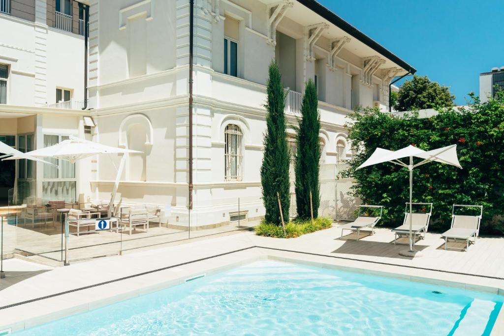 里米尼的住宿－Hotel Regina Elena 57 & Oro Bianco SPA，一座带椅子和遮阳伞的大楼前的游泳池