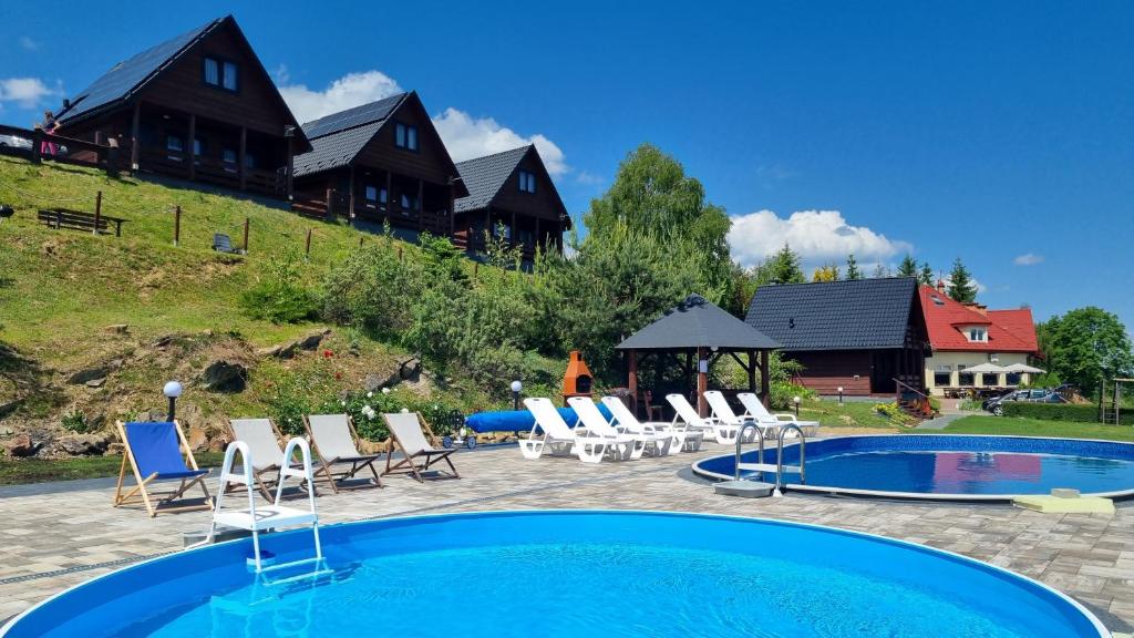 uma piscina com cadeiras e uma casa ao fundo em Na Górce - Domki z Widokiem Na Jezioro i Góry em Polańczyk